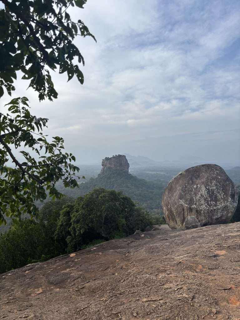 Sigiriya, the ancient rock fortress in Sri Lanka, stands majestically with its towering rock formation, surrounded by lush greenery and remnants of historical frescoes.