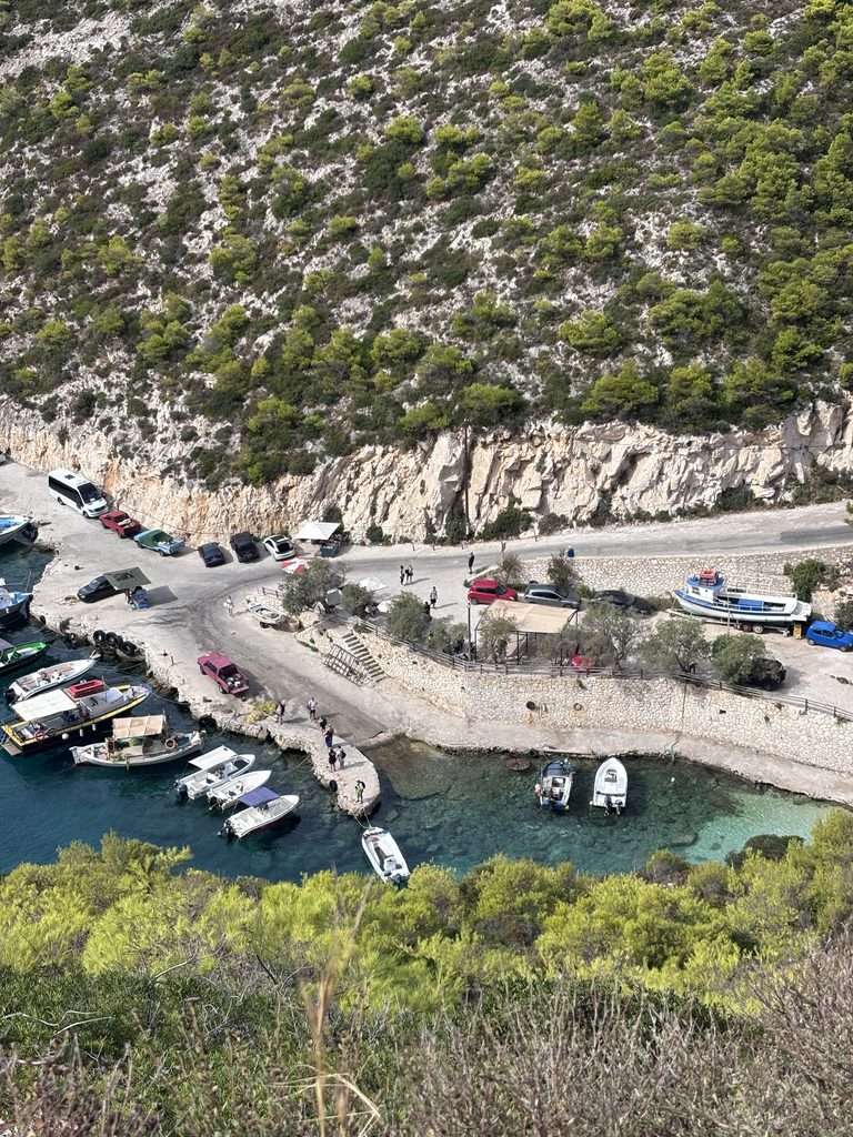 View overlooking a small harbour in Zante, with boats moored in clear turquoise water and a coastal road beside the rocky cliffs