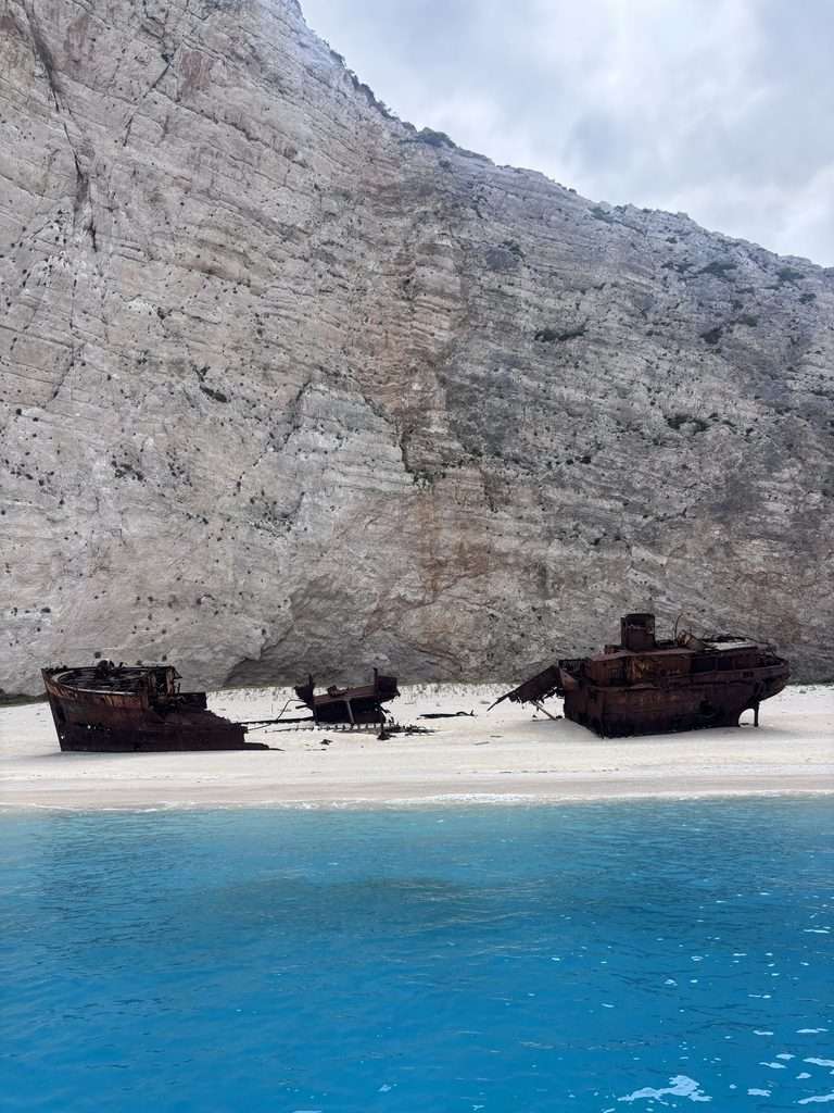 shipwreck Beach in Zante viewed from the boat, showing the white sandy beach, towering limestone cliffs and turquoise sea during a Zante shipwreck boat tour.